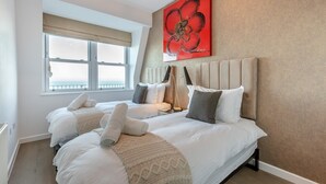 A hotel room with two beds, a large window with a view, a red floral artwork on the wall, and a modern lamp. - 2 Bed in Ilfracombe (oc-o30532) (Ilfracombe)