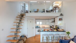A modern kitchen with a central island, wooden staircase, and a dining area with bar stools. - 2 Bed in Ilfracombe (oc-o30532) (Ilfracombe)