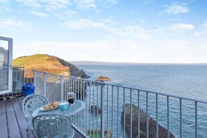 A deck with a table and chairs overlooking a coastal view with rocky cliffs and the sea.