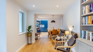Ein modernes Wohnzimmer mit Essbereich, einer Bücherwand und einer Küche im Hintergrund.