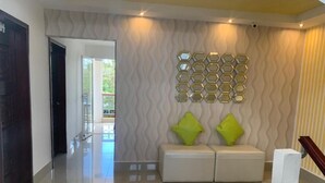 A modern lobby with a wavy textured wall, a seating area with two white cushioned benches, and a decorative hexagonal mirror wall. - Hotel Tijerinos (Boaco)