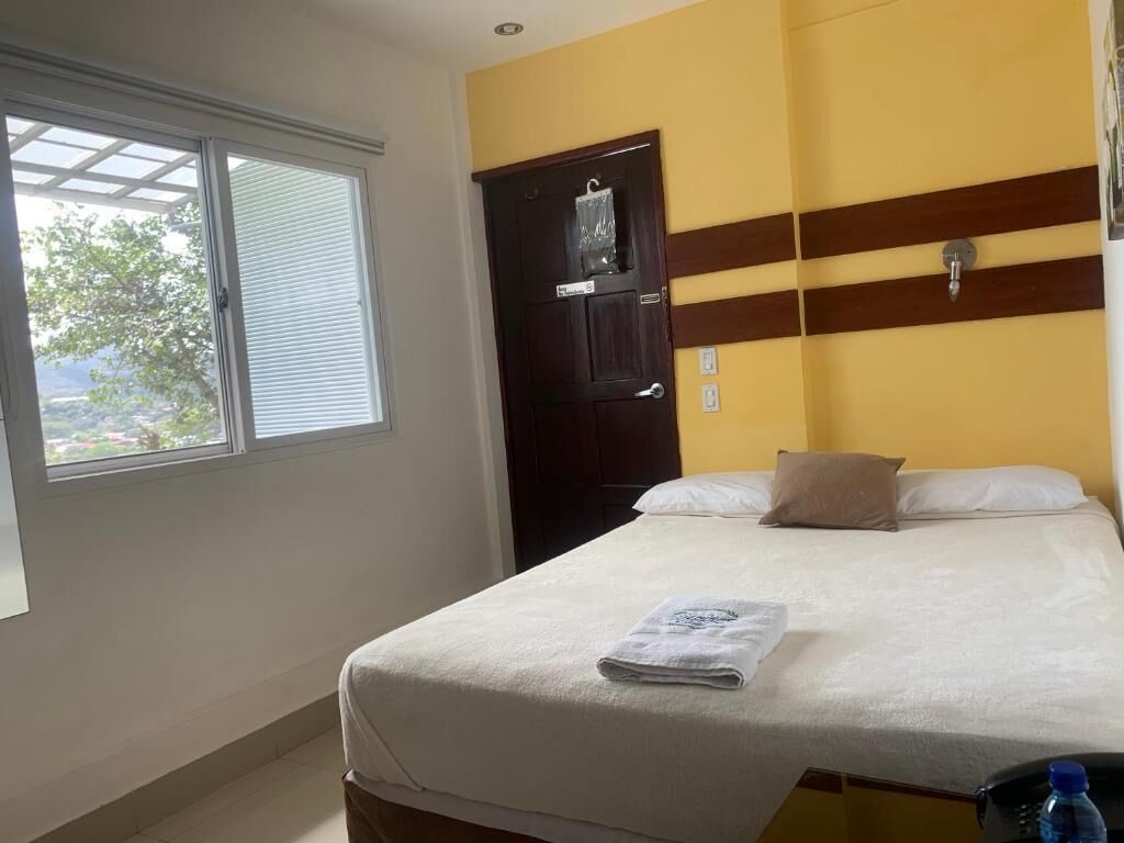 A hotel room with a bed, a window, a wardrobe, and a wall-mounted shelf.