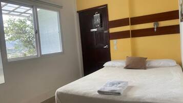A hotel room with a bed, a window, a wardrobe, and a wall-mounted shelf.