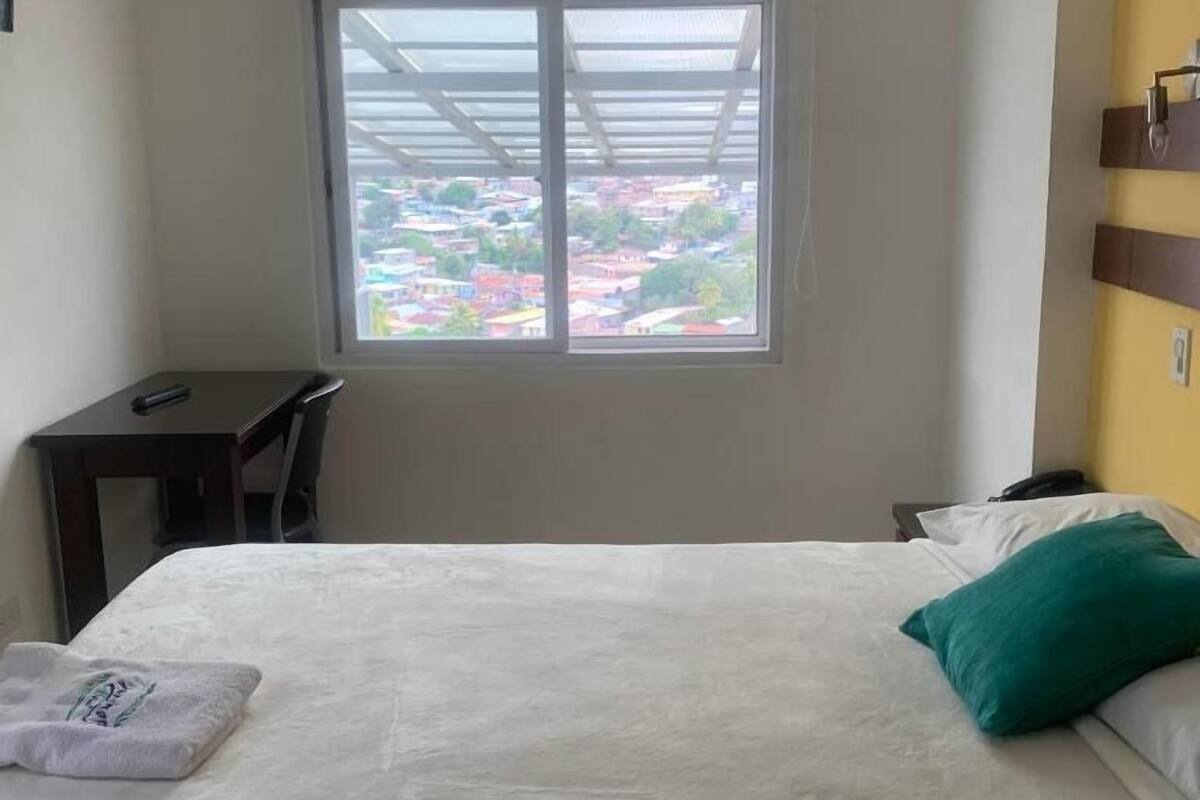 A hotel room with a bed, a desk, and a window with a view of buildings.