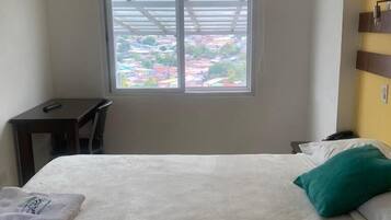 A hotel room with a bed, a desk, and a window with a view of buildings.