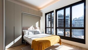 Un dormitorio moderno con un ventanal grande, una cama con un plaid color mostaza y almacenamiento integrado.