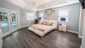 A bedroom with a curved bed, a chandelier, a nightstand, and a view of a swimming pool. - All Amenities of home! Centrally located, family friendly & ideal entertaining (Port St. Lucie)