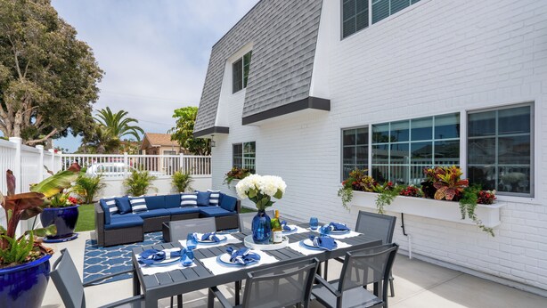 A patio with a dining table set for four, surrounded by chairs, a blue sofa, and a white fence. - Stunning Family Getaway - One Block from Beach, Fast WiFi, A/C, BBQ, Parking (San Diego)