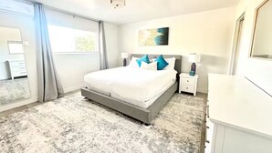 A bedroom with a large bed, a nightstand, a dresser, a ceiling light, and a window with curtains. - Stunning Family Getaway - One Block from Beach, Fast WiFi, A/C, BBQ, Parking (San Diego)