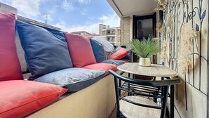 Un balcon avec un canapé, des coussins, une petite table et une plante en pot.