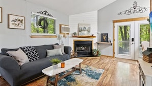 A living room with a fireplace, a sofa, a coffee table, and a door leading to a balcony. - Wildflower (Sautee Nacoochee)
