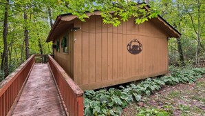 A wooden cabin with a small porch and a wooden bridge leading to it, surrounded by lush greenery. - Wildflower (Sautee Nacoochee)