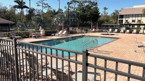 Ein rechteckiger Pool mit einem Metallzaun, umgeben von Liegestühlen und einer gepflasterten Terrasse.