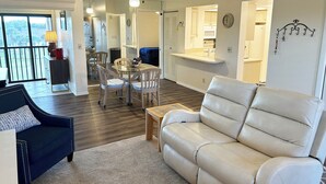 Ein modernes Wohnzimmer mit einem weißen Ledersofa, einem dunkelblauen Sessel und einem Essbereich mit Tisch und Stühlen.