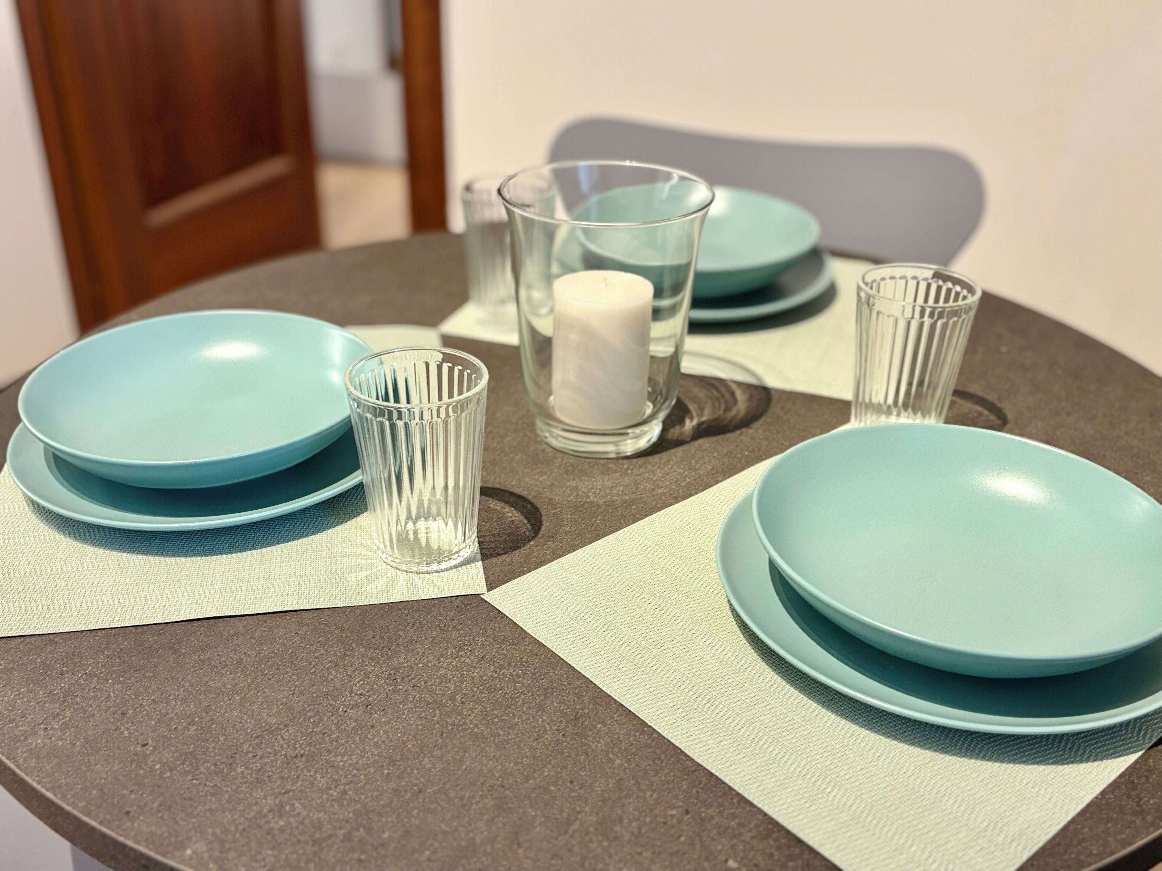 A table set with blue plates, a clear glass, and a white candle.