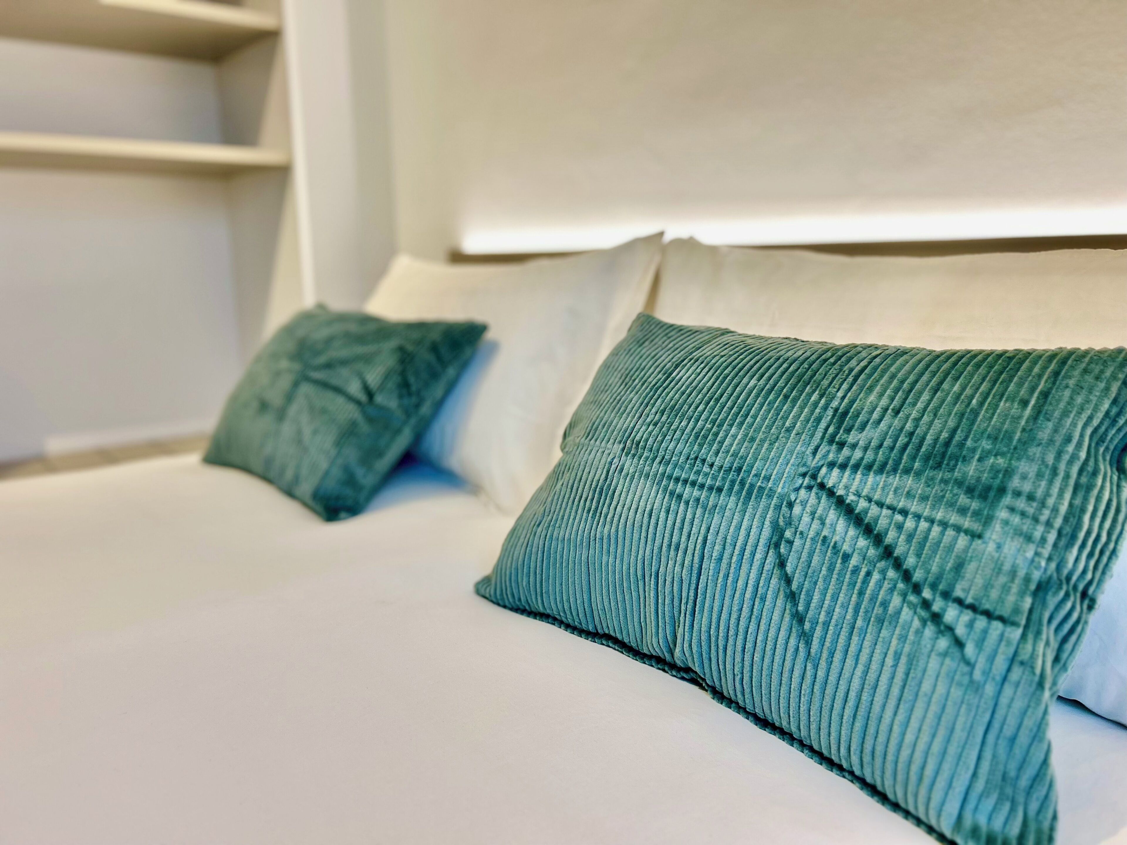 Ein Bett mit zwei grünen Kissen und einem weißen Kopfteil.
