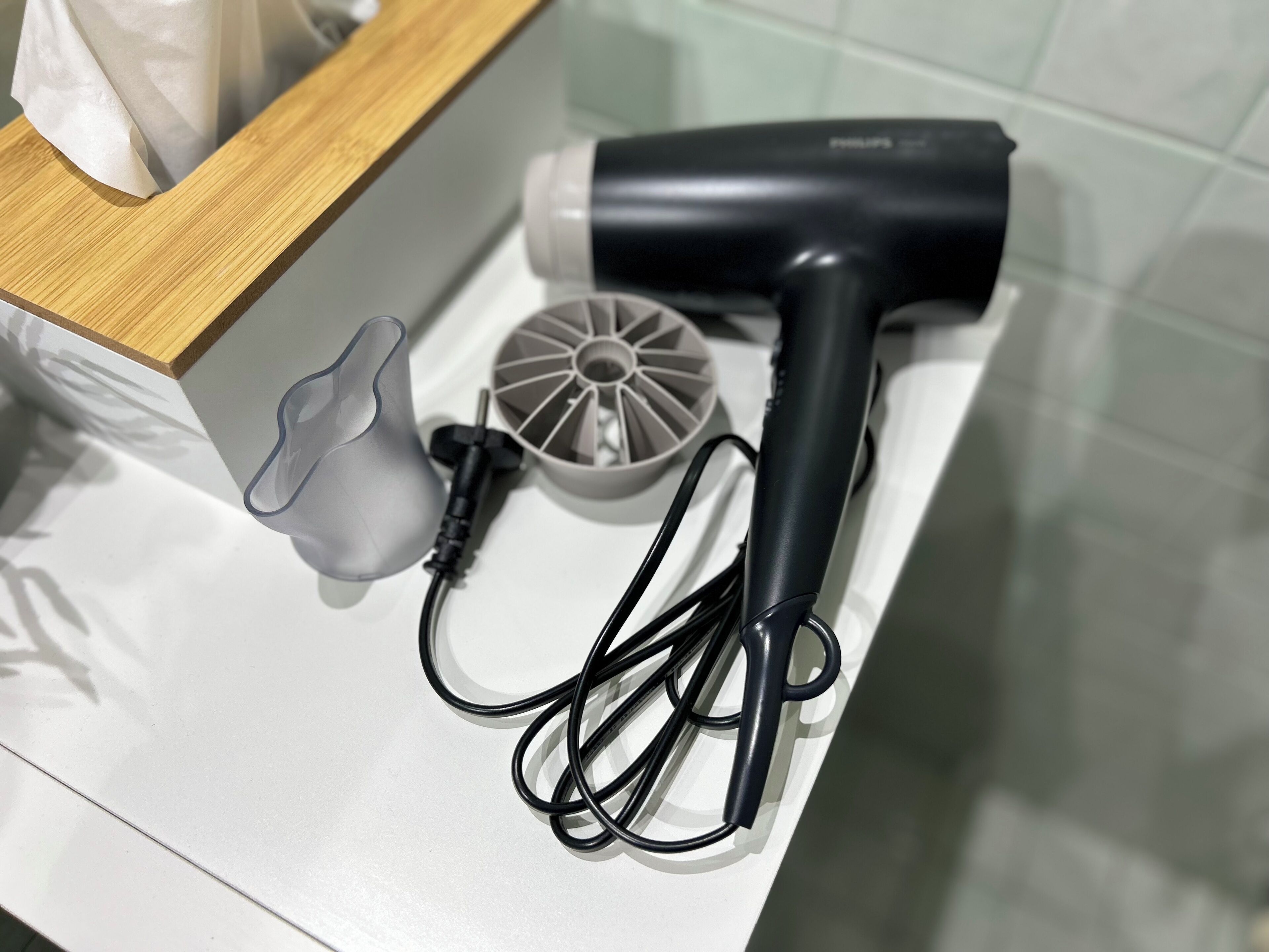 Un sèche-cheveux, un câble d’alimentation et une prise électrique sur une surface blanche.