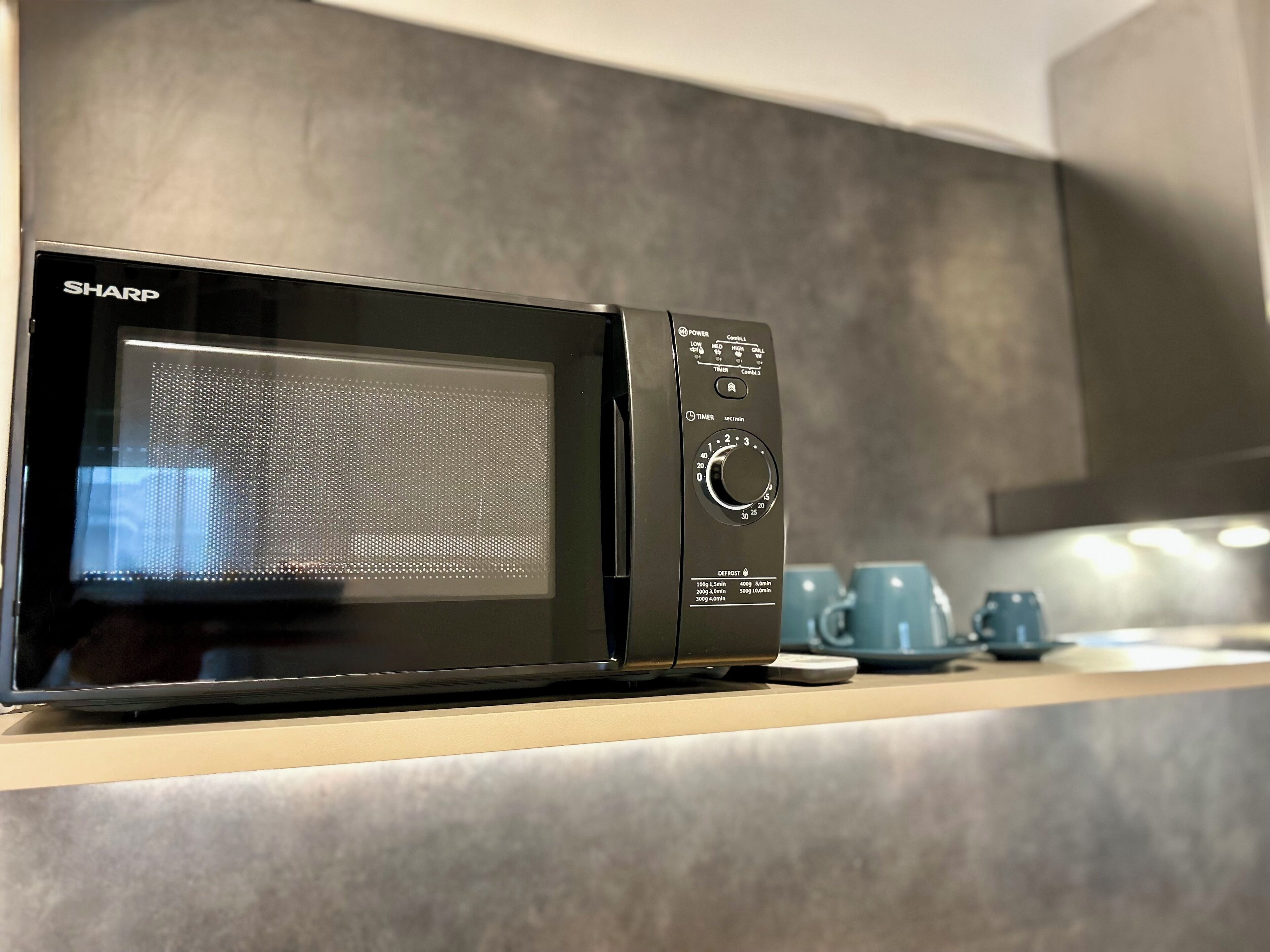 Een zwarte Sharp magnetron met een digitaal display en timerinstellingen op een keukentafel.