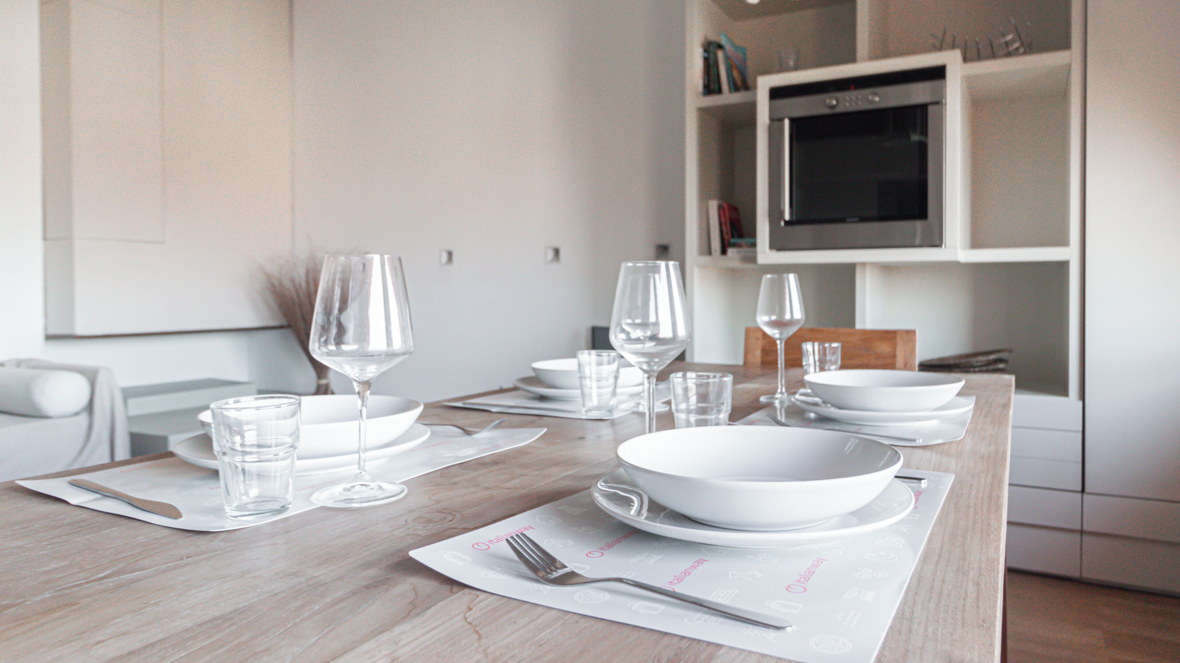 A dining table set with white plates, bowls, glasses, and cutlery.