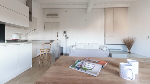 A modern, minimalist bedroom with a large bed, a bedside table, and a magazine on the floor.