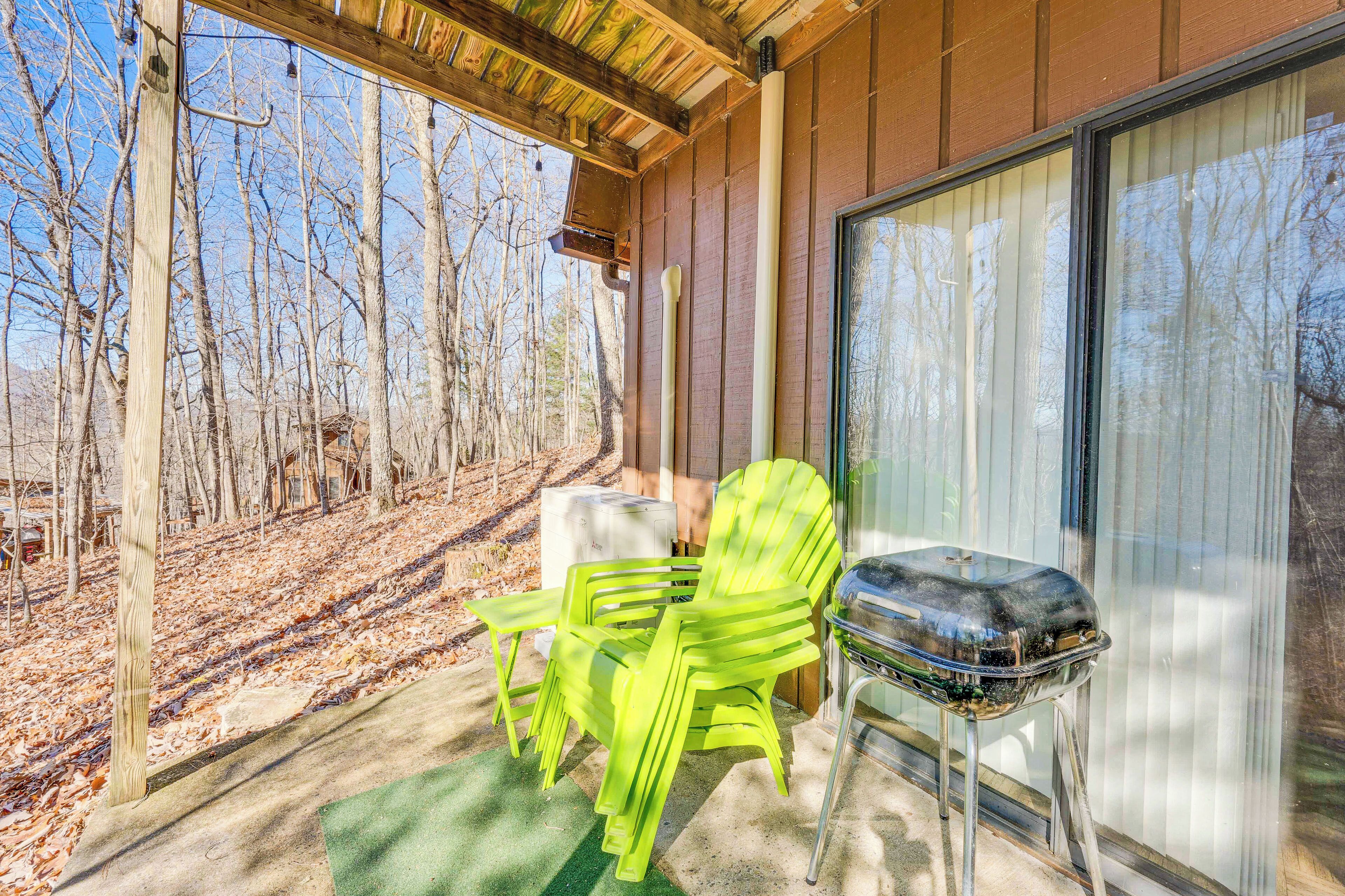 A covered outdoor seating area with a grill and chairs, overlooking a forested area.
