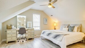 Une chambre avec un plafond en pente, un lit agrémenté d’oreillers à motifs, un bureau avec un miroir et un ventilateur de plafond.