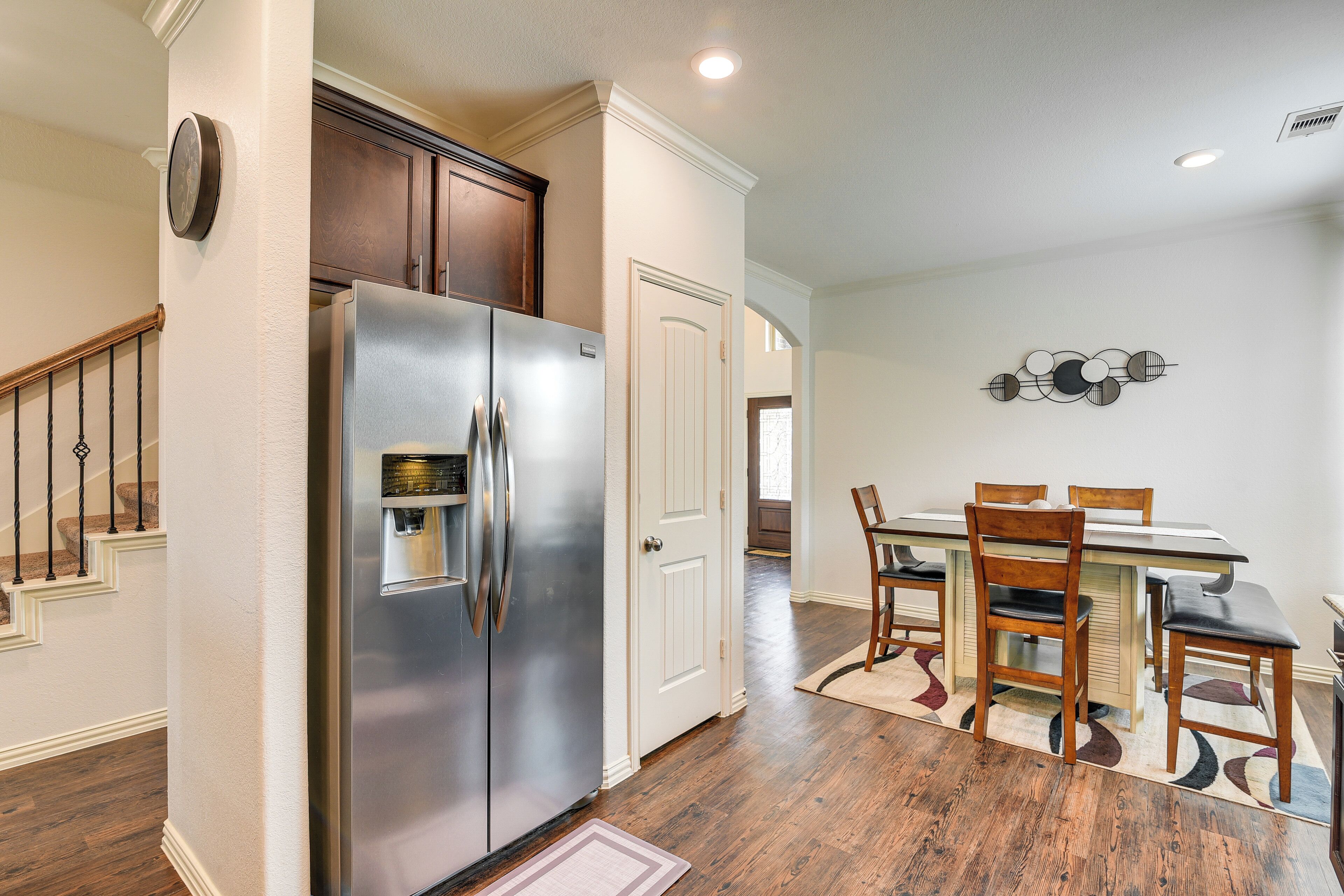 A kitchen with a stainless steel refrigerator, wooden cabinets, a dining table with chairs, and a rug.