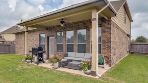 Una casa de ladrillo con un porche cubierto, muebles de exterior y una parrilla.