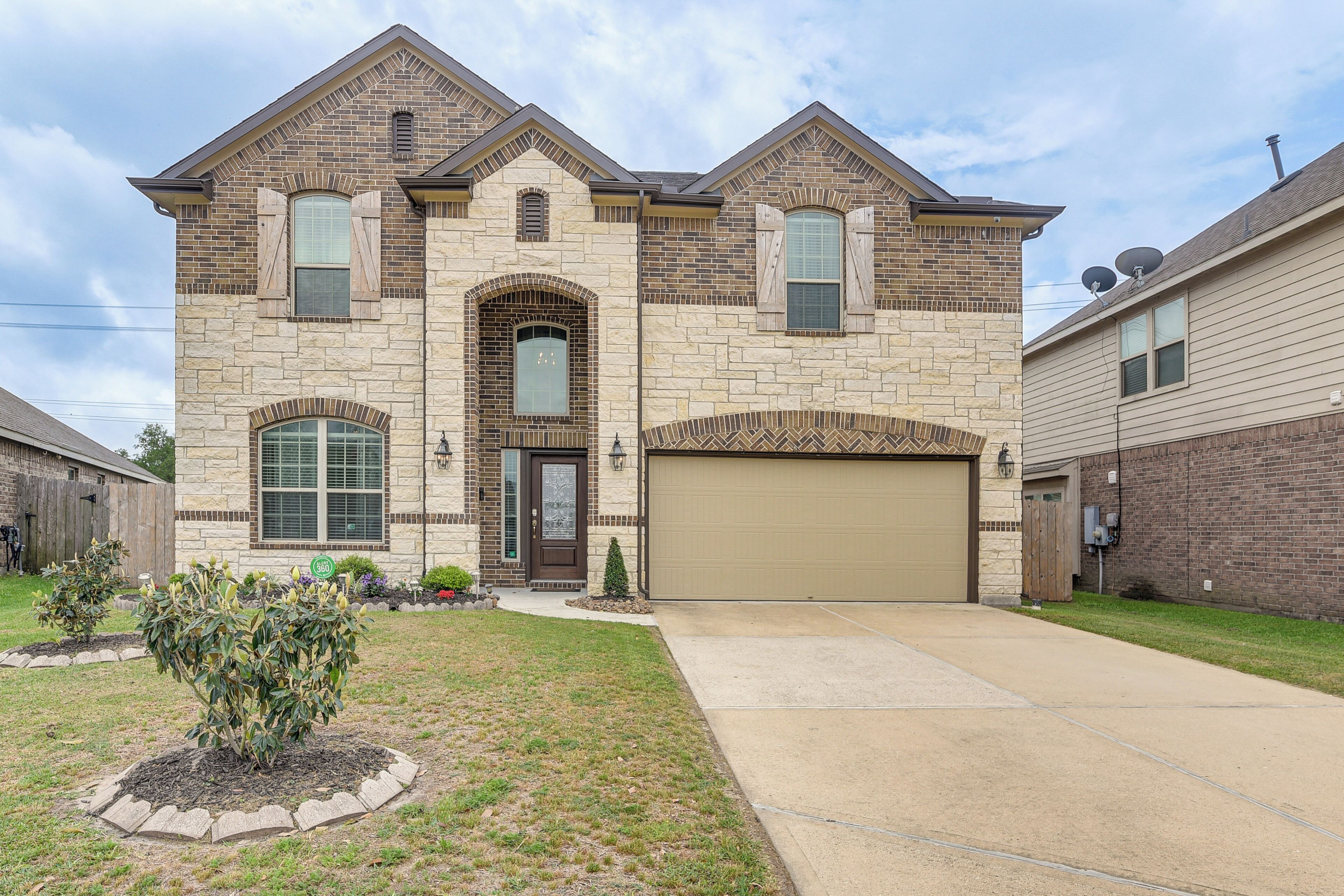 A two-story house with a garage, stone facade, and a small front yard with a tree.