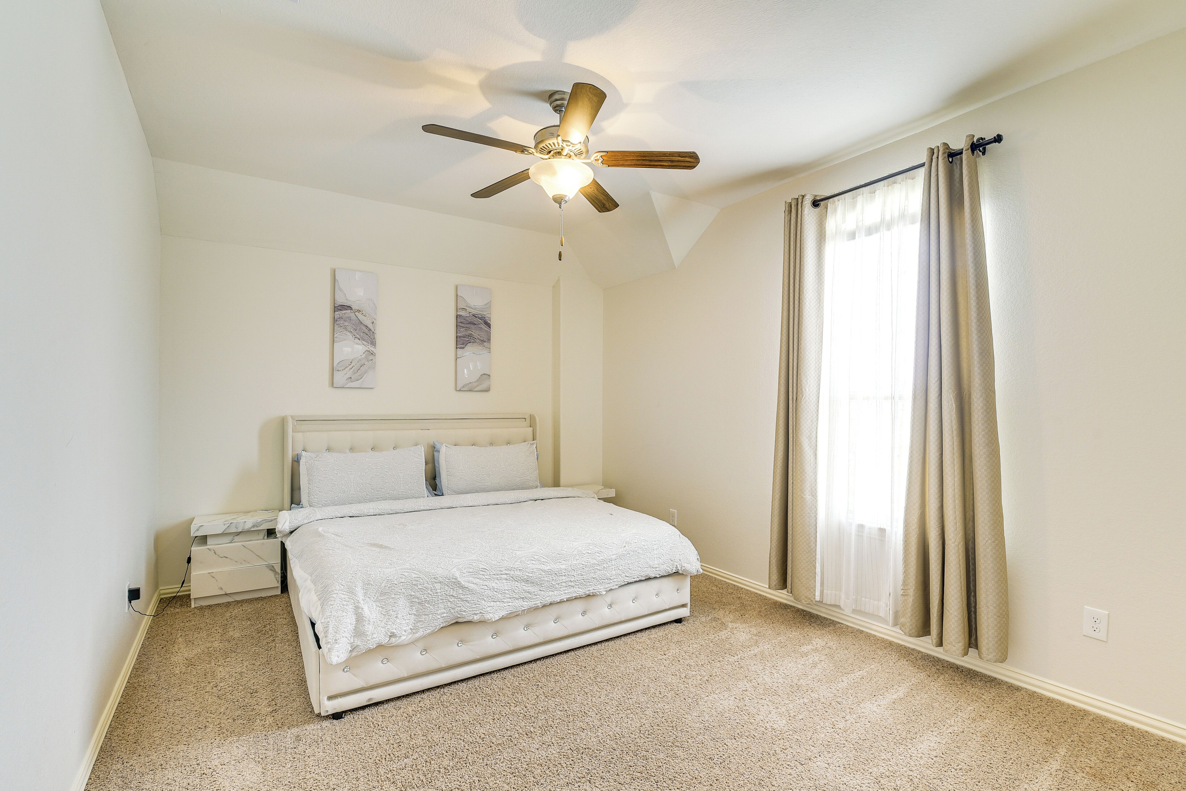 A bedroom with a bed, ceiling fan, and large window with curtains.