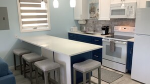 Una cocina moderna con una isla central, taburetes de bar, microondas, horno y fregadero.