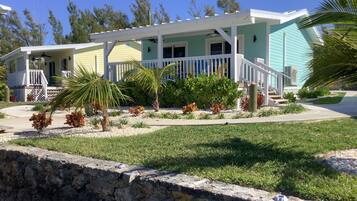 A two-story house with a porch, a small garden with palm trees, and a stone retaining wall.