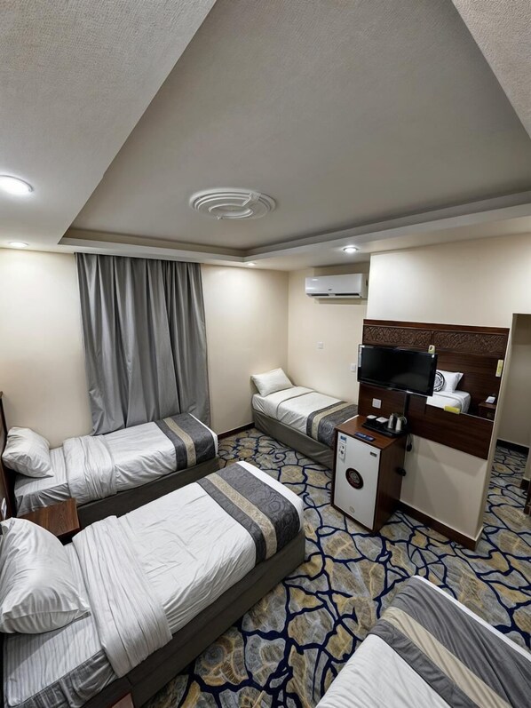 A hotel room with three beds, a desk with a TV, and an air conditioning unit on the wall. - Aljumeza Tower (Makkah)