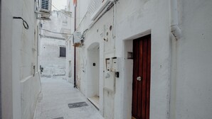 A narrow, white-walled alleyway with a red door on the right, a small window on the left, and a metal grate on the floor. - Casa Lucia by Monholiday (Monopoli)