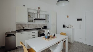 A compact kitchen with white cabinetry, a built-in oven, and a dining area with a white table and chairs. - Casa Lucia by Monholiday (Monopoli)