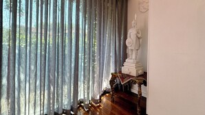 Ein Zimmer mit einem großen Fenster, Holzboden, einer Statue und einer weißen Wand.