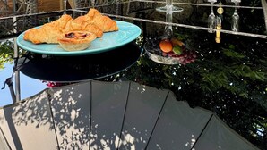 Ein Essbereich im Freien mit einem Tisch für zwei Personen, gedeckt mit Croissants, Obst und einer Flasche Champagner.