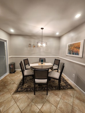 A dining area with a round table, six chairs, a chandelier, a painting, and a heater.