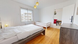 Un dormitorio con una cama de madera, una ventana, un pequeño banco y una zona de comedor con una silla roja.