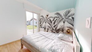 Un dormitorio con una cama, una puerta corrediza de vidrio al exterior y una pared con un mural de hojas tropicales.