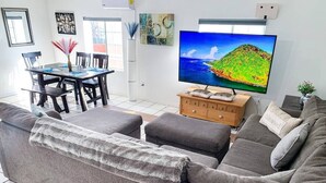 Una sala de estar con un sofá gris, televisor, aparador de madera y una mesa de comedor con sillas.
