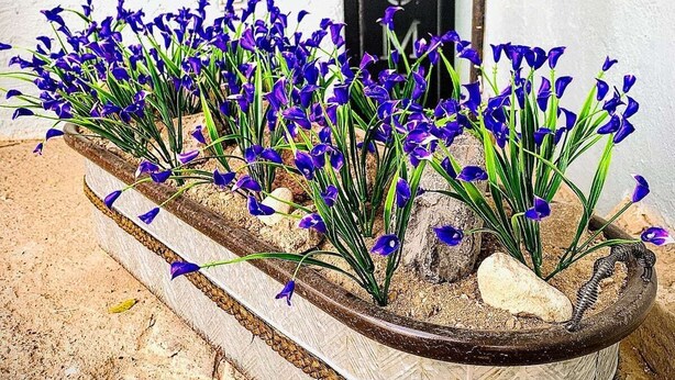 Un cartel de bienvenida con una puerta de metal rústica y una maceta con flores moradas.