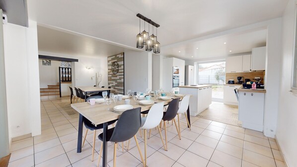 A modern kitchen with white cabinets, a dining area with a wooden table and chairs, and a staircase leading to another level.