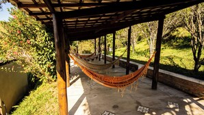 A hammock under a wooden pergola with a view of a garden and a body of water. - Hotel Fazenda Bavária (Pouso Alto)