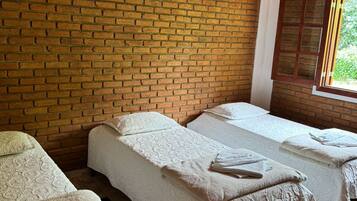 Two beds with crisp linens and towels are arranged in this cozy space, featuring a brick wall and a ceiling above.