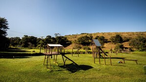 A grassy field with playground equipment and a hill in the background. - Hotel Fazenda Bavária (Pouso Alto)