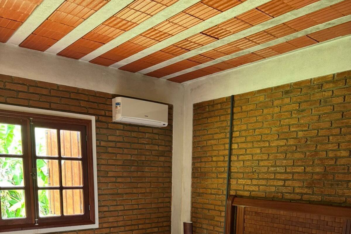 Une pièce avec un lit en bois, un mur en briques, une fenêtre avec des stores et un appareil de climatisation.