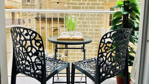 Un balcon avec deux chaises en métal noir, une petite table ronde et un pot de fleurs.