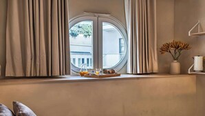 Un dormitori amb un llit, una finestra amb cortines, una bandeja amb articles per esmorzar i un vas amb flors sobre una estant.