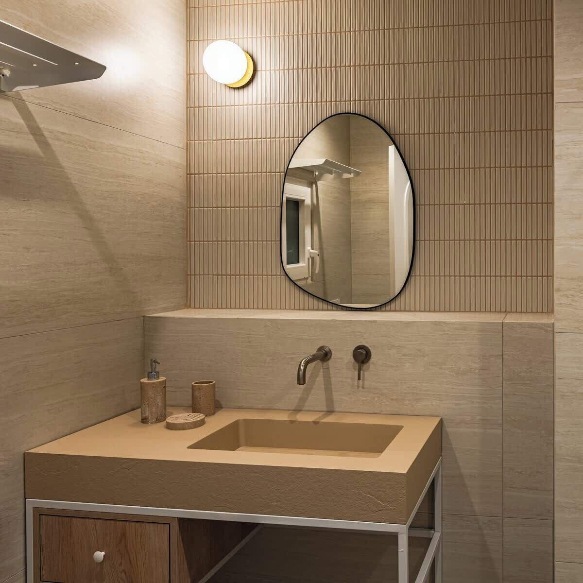 A modern bathroom with a beige sink, a round mirror, and a wall-mounted light fixture.